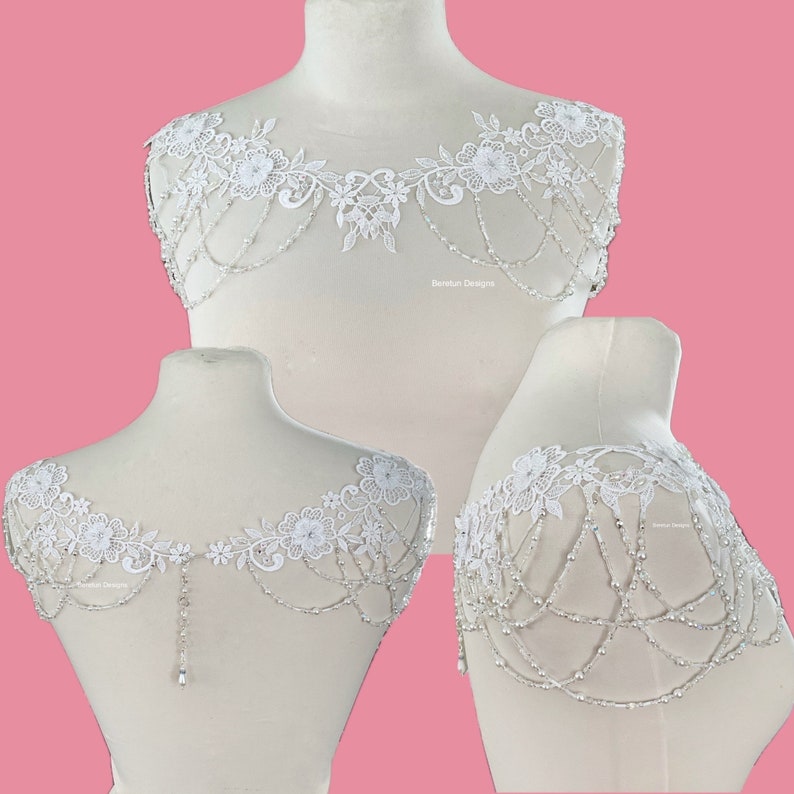 May include: White lace bridal shoulder piece with beaded chains and floral accents. The piece is shown on a white mannequin.