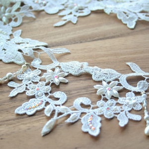 May include: White lace trim with pearl and rhinestone embellishments. The lace features a floral design with delicate leaves and intricate details.