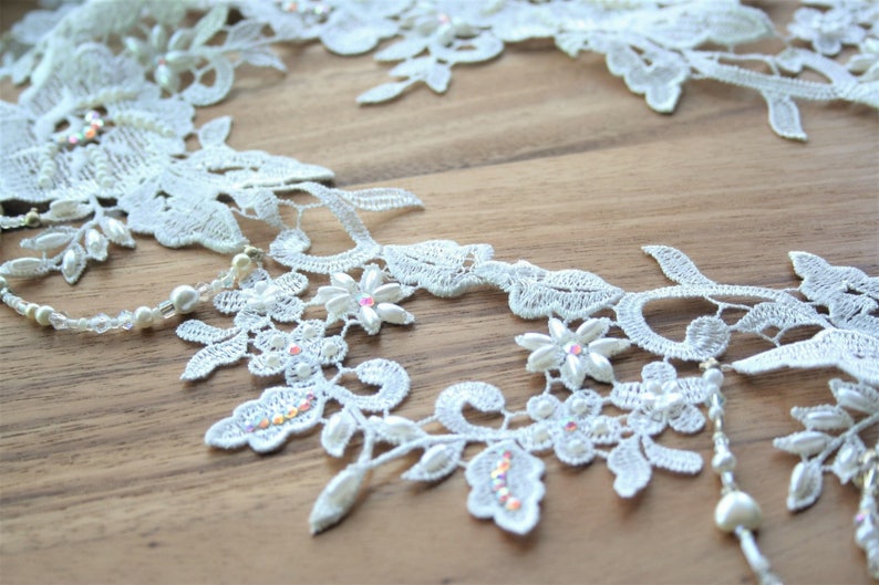 May include: White lace trim with pearl and rhinestone embellishments. The lace features a floral design with delicate leaves and intricate details.