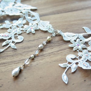 May include: White lace choker necklace with pearl and crystal accents. The necklace has a delicate floral design and features a dangling pearl drop.