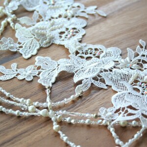 May include: White lace trim with pearl and crystal beads. The lace features a floral design.