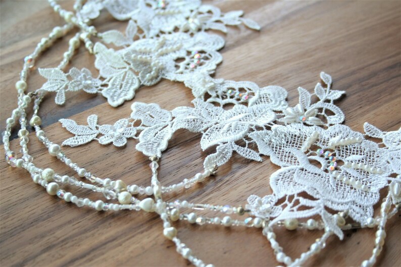 May include: White lace trim with pearl and crystal beads. The lace features a floral design.