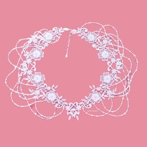 May include: A white lace necklace with a delicate floral design and multiple strands of pearls. The necklace is arranged in a heart shape and has a simple clasp.