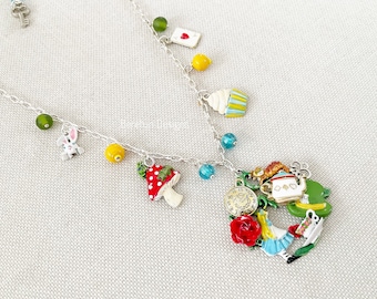 Può includere: Una collana d'argento con più ciondoli, tra cui un fungo, un cupcake, una carta da gioco, un coniglio, una teiera, un orologio e una rosa rossa. I ciondoli sono tutti colorati e fantasiosi.