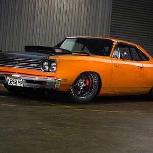 May include: A bright orange 1968 Plymouth Road Runner with a black hood and a license plate that reads "1600 HP".