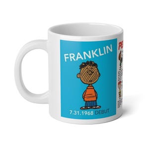 Peut inclure: Un mug en céramique blanche avec un graphique rectangulaire bleu représentant le personnage Franklin des Peanuts. Le texte indique FRANKLIN et 7.31.1968 DEBUT. À droite, une liste verticale partielle d'autres personnages avec du texte est visible.