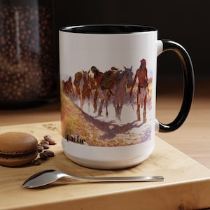 May include: White ceramic mug with a black handle and rim. The mug features a detailed illustration of Native Americans on horseback, with the word "Apache" printed on the side.