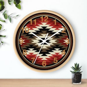 May include: Round wall clock with a light wood frame. The clock face features a geometric pattern in red, black, cream, and brown. Gold-colored numerals mark the hours. The clock hands are white.