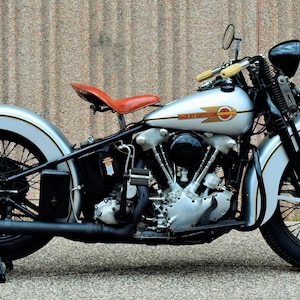 May include: A silver and black Harley Davidson motorcycle with a brown leather seat. The motorcycle has a chrome headlight and a chrome exhaust pipe.