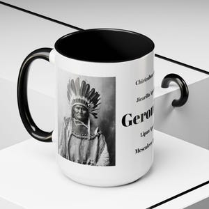 May include: White ceramic mug with a black interior and handle. The mug features a black and white portrait of Geronimo, with text that includes his name and the names of several Apache tribes.