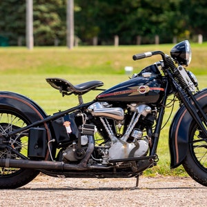 Puede incluir: Una motocicleta Harley Davidson negra de la década de 1930 con detalles cromados y un asiento de cuero marrón. La motocicleta tiene un guardabarros delantero grande y un guardabarros trasero más pequeño.