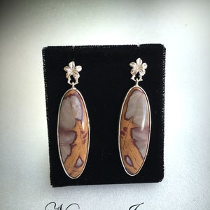 May include: A pair of silver earrings with a brown and white Noreena Jasper stone. The earrings have a flower design at the top.