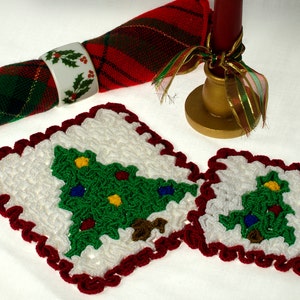 May include: Two white crocheted Christmas tree coasters with red trim. The coasters feature green, red, blue, and yellow yarn details.