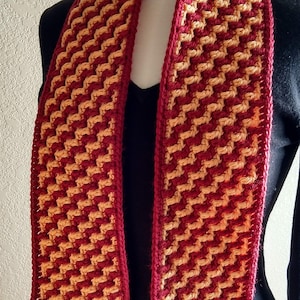 May include: A crocheted scarf with a geometric pattern in shades of red and orange.
