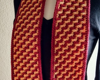 May include: A crocheted scarf with a geometric pattern in shades of red and orange.