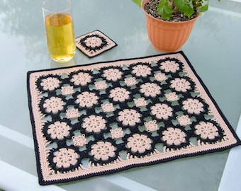 May include: A black and beige crocheted table runner with a floral pattern. The runner is on a glass table top.