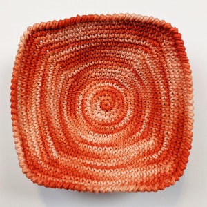 May include: A crocheted bowl with a circular pattern in shades of orange and peach.