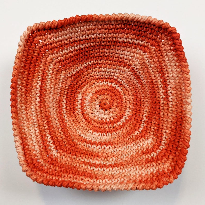 May include: A crocheted bowl with a circular pattern in shades of orange and peach.