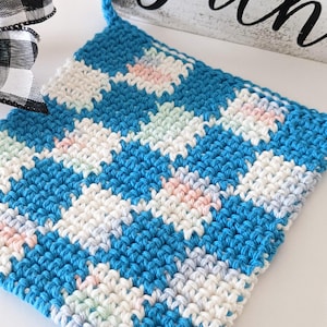May include: A blue, white, and pastel-colored crocheted dishcloth with a checkered pattern.