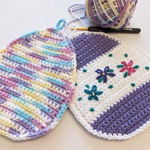 May include: Two crocheted egg-shaped hot pads. One is a multi-colored striped design in shades of pink, yellow, blue, and white. The other is white with a purple stripe and embroidered flowers in shades of pink, purple, and green.