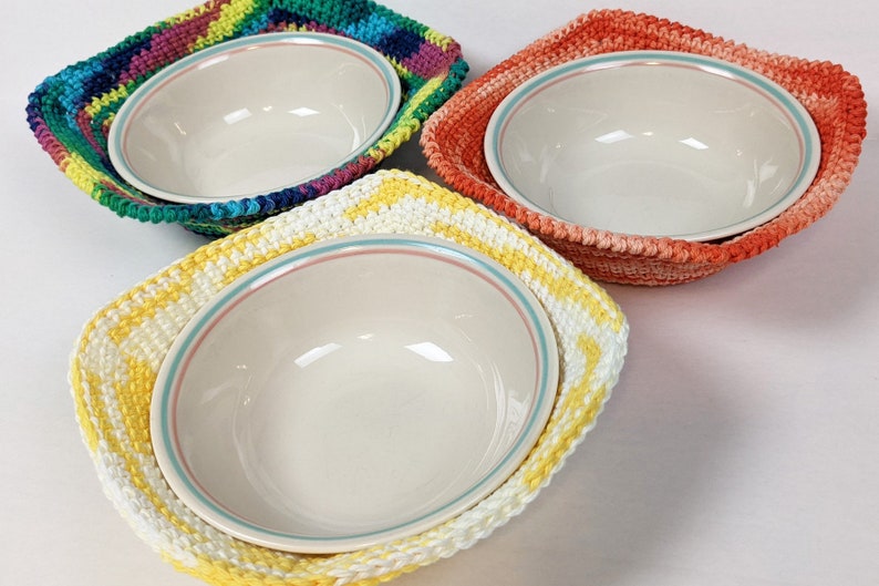 May include: Three crocheted bowl cozies in different colors. The cozies are square shaped and feature a colorful, striped design. The cozies are made with a soft yarn and are perfect for protecting bowls from scratches and heat.