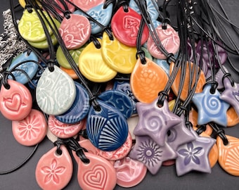 May include: A collection of ceramic pendants with various designs and colours, including blue, green, pink, purple, and yellow. Each pendant is attached to a black cord.