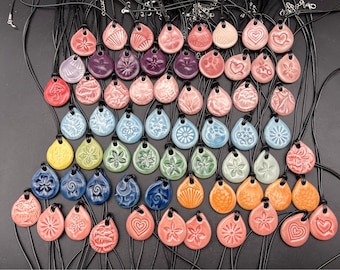 May include: A collection of 50 ceramic pendants with various designs and colours, hanging on black cords. The pendants are in the shape of teardrops and feature floral, geometric, and abstract patterns.