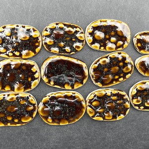 Puede incluir: Doce azulejos de cerámica de forma ovalada con un esmalte moteado marrón y dorado. Los azulejos tienen una superficie texturizada y están dispuestos en tres filas de cuatro.