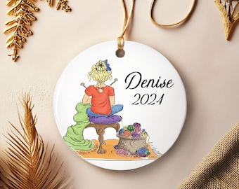 May include: A round ceramic ornament featuring a woman knitting, with the name "Denise" and the year "2024" printed on it. The woman is wearing a red shirt and blue pants. A basket of yarn is next to her.