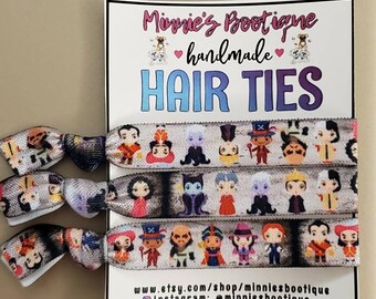 May include: Set of four colorful hair ties featuring a variety of Disney villains. The hair ties are made of elastic fabric and have a white background with colorful cartoon images of villains like Ursula, Cruella de Vil, and Maleficent. The hair ties are packaged with a white card that says "Minnie's Boutique handmade Hair Ties" and includes contact information for the shop.