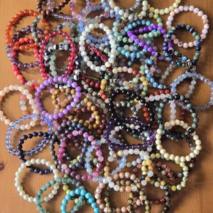 Peut inclure: Une grande collection de bracelets circulaires en perles disposés en grappe. Les bracelets sont composés de divers types de perles en pierre polie et en verre dans un large spectre de couleurs, notamment le bleu, le violet, le vert, le rouge, le blanc et le marron.