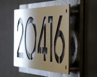 May include: A gold metal house number plaque with the number 20416 cut out. The plaque is mounted on a gray wall.