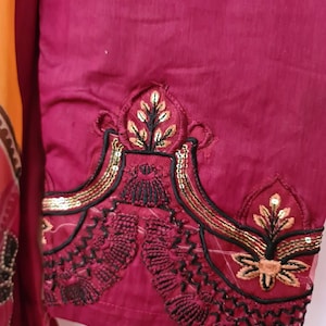May include: A close-up of a maroon fabric with black and gold embroidery. The embroidery features a floral design with sequins.