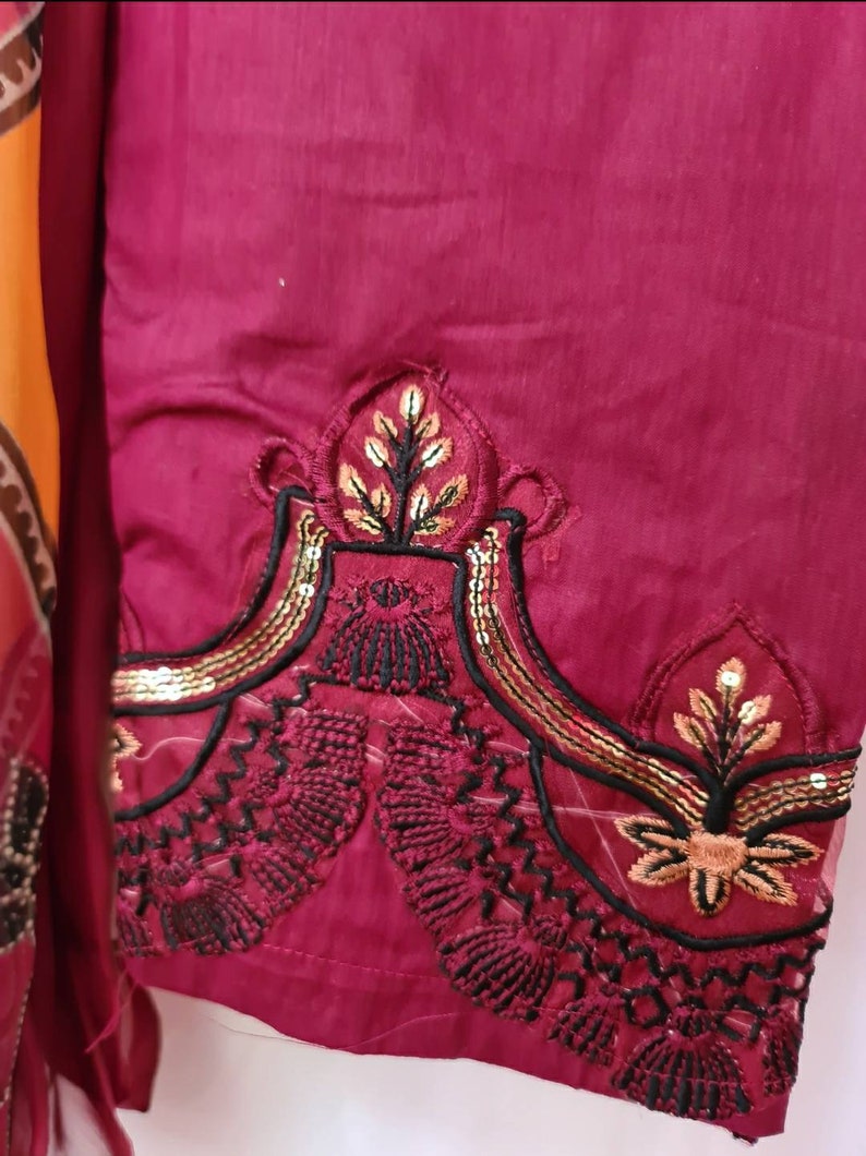 May include: A close-up of a maroon fabric with black and gold embroidery. The embroidery features a floral design with sequins.