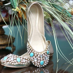 May include: A pair of gold flat shoes with turquoise and white embellishments. The shoes are decorated with pearls and rhinestones.