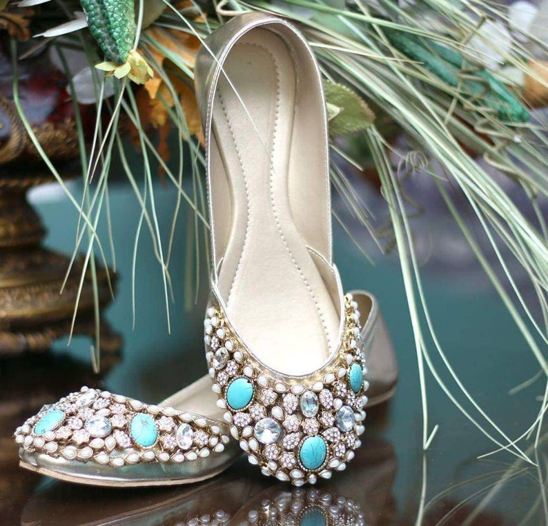 May include: A pair of gold flat shoes with turquoise and white embellishments. The shoes are decorated with pearls and rhinestones.