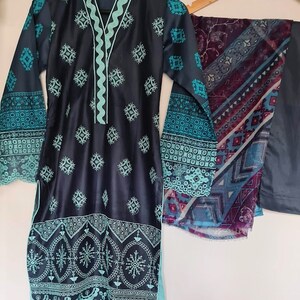 May include: A dark blue and teal patterned dress with a matching teal scarf. The dress has a V-neckline and long sleeves with a decorative trim. The scarf has a geometric pattern.