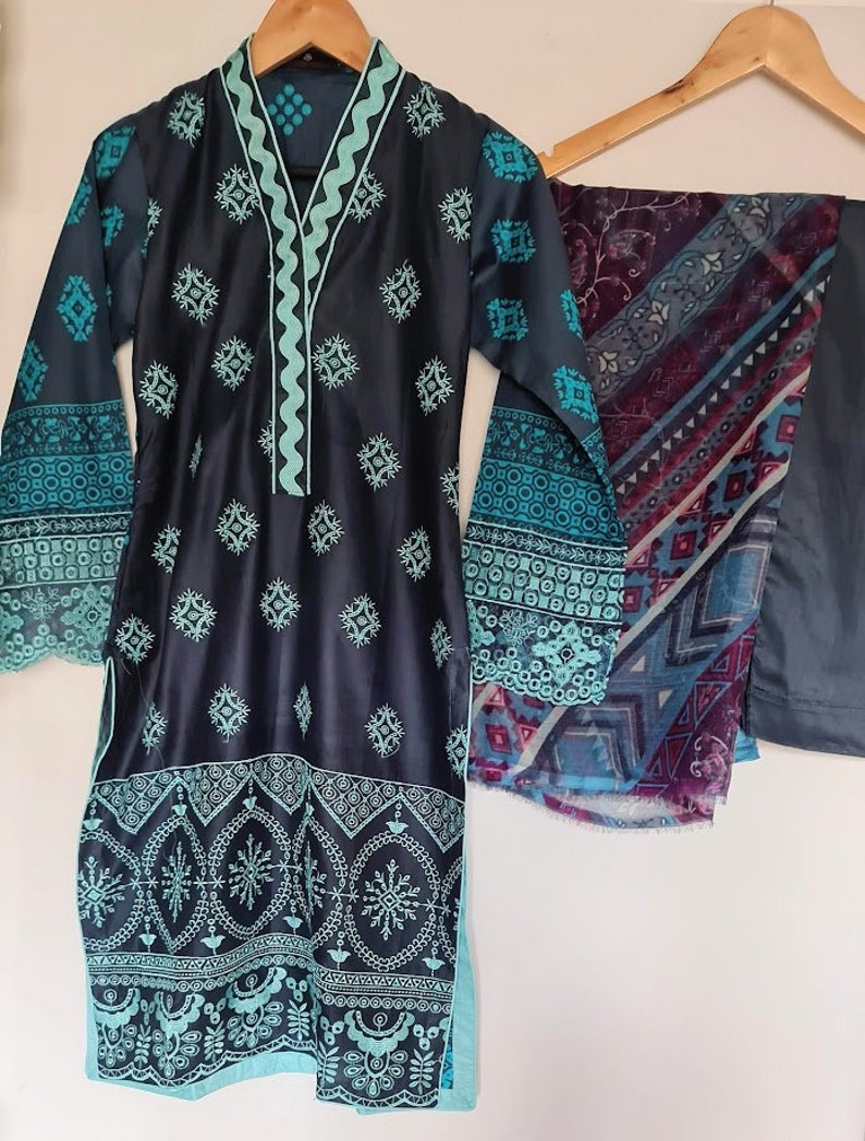 May include: A dark blue and teal patterned dress with a matching teal scarf. The dress has a V-neckline and long sleeves with a decorative trim. The scarf has a geometric pattern.
