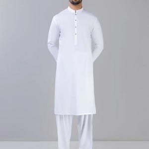 May include: A white long-sleeved shirt with a mandarin collar and a single button closure. The shirt is paired with white pants.