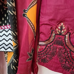 May include: A maroon fabric with black and gold embroidery. The fabric has a geometric pattern and a floral design.