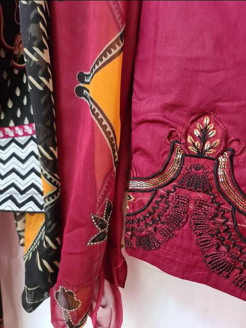 May include: A maroon fabric with black and gold embroidery. The fabric has a geometric pattern and a floral design.