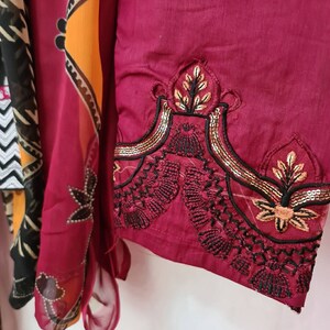 May include: A maroon fabric with black and gold embroidery. The embroidery features a floral design with sequins.