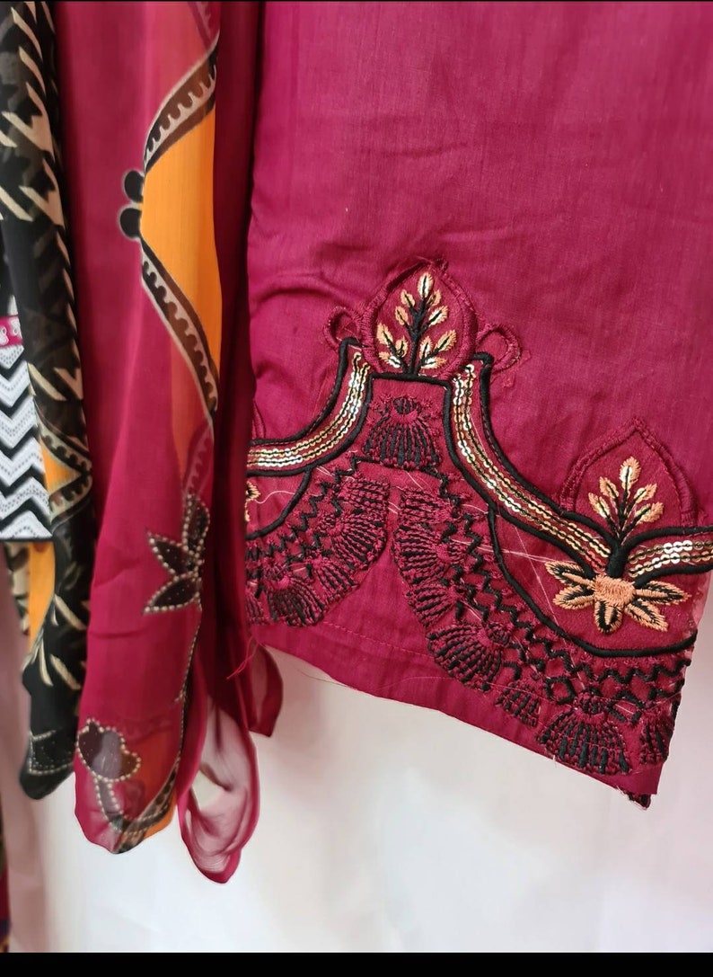 May include: A maroon fabric with black and gold embroidery. The embroidery features a floral design with sequins.