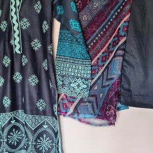 May include: A dark blue and teal embroidered dress with a matching dupatta and pants. The dress has a V-neckline and a floral pattern. The dupatta has a geometric pattern. The pants are solid dark blue.