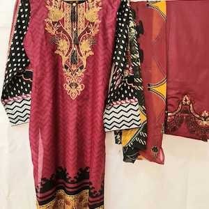 May include: A maroon and black printed three-piece dress set with a long-sleeved top, a matching bottom, and a dupatta. The top features a floral design with gold embroidery and a tassel. The bottom has a chevron pattern and the dupatta has a floral design with gold accents.