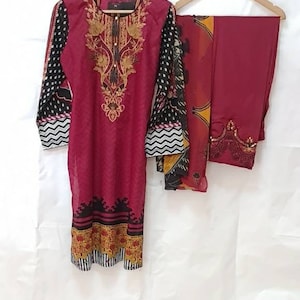 May include: A maroon three-piece women's clothing set with black and white polka dot and chevron patterns, gold embroidery, and a maroon dupatta.