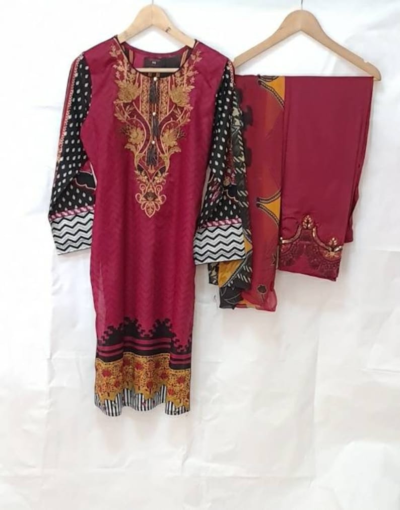 May include: A maroon three-piece women's clothing set with black and white polka dot and chevron patterns, gold embroidery, and a maroon dupatta.