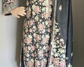 Op de afbeelding: Een zwarte jurk met bloemenprint en een bijpassende zwarte sjaal. De jurk heeft een V-hals en lange mouwen. De sjaal heeft een bloemenrand.
