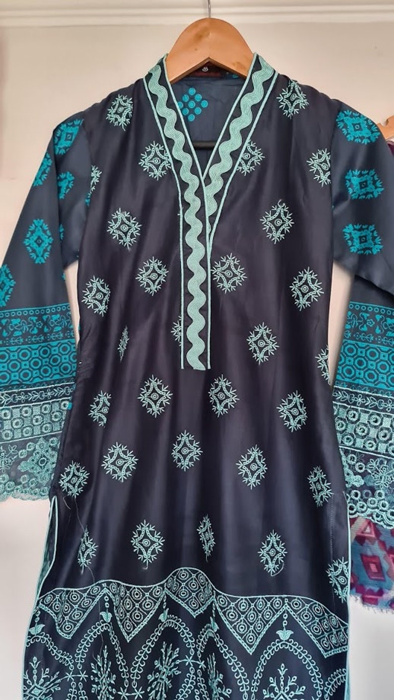 May include: A dark blue tunic with a teal embroidered neckline and geometric patterns. The tunic has long sleeves with a teal embroidered border and a teal embroidered hem.