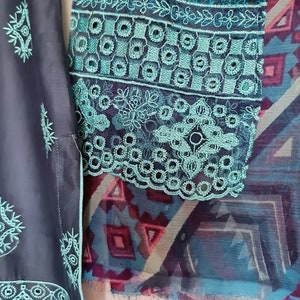 May include: A teal and black fabric with intricate embroidery. The fabric has a geometric pattern and a floral design. The fabric is trimmed with a lace border.